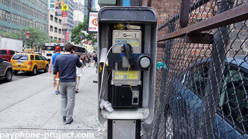 A payphone rots as a cell-phone user strolls past. 42nd Street.