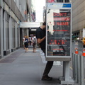 Holding the phone on his shoulder, an address book in his left hand, while dialing the phone with his right hand.