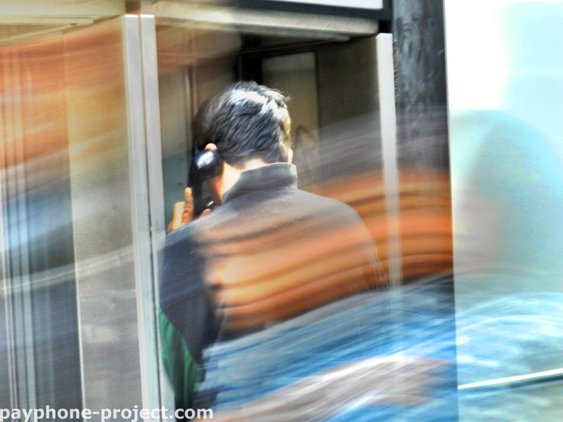 Talking on a midtown payphone as a blur of humanity passes by